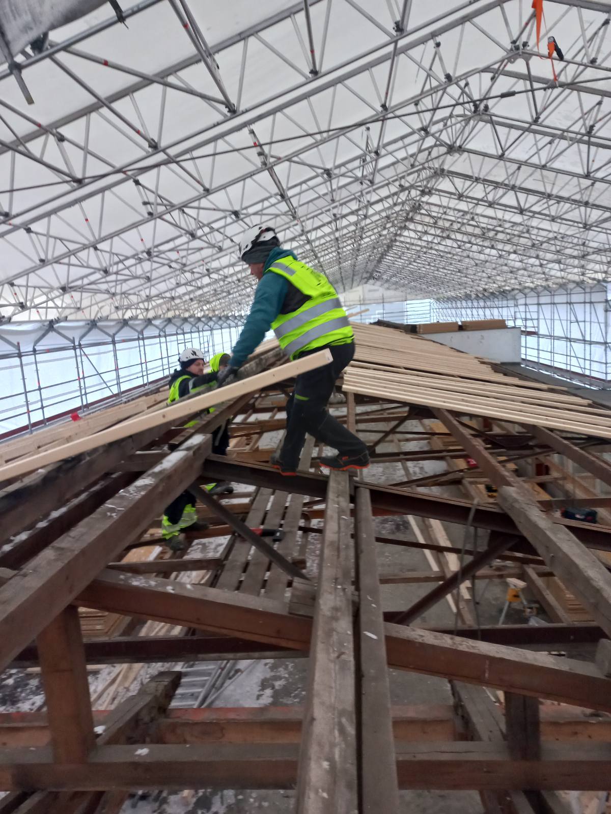 Workers on a timber roof under a temporary scaffolding tent